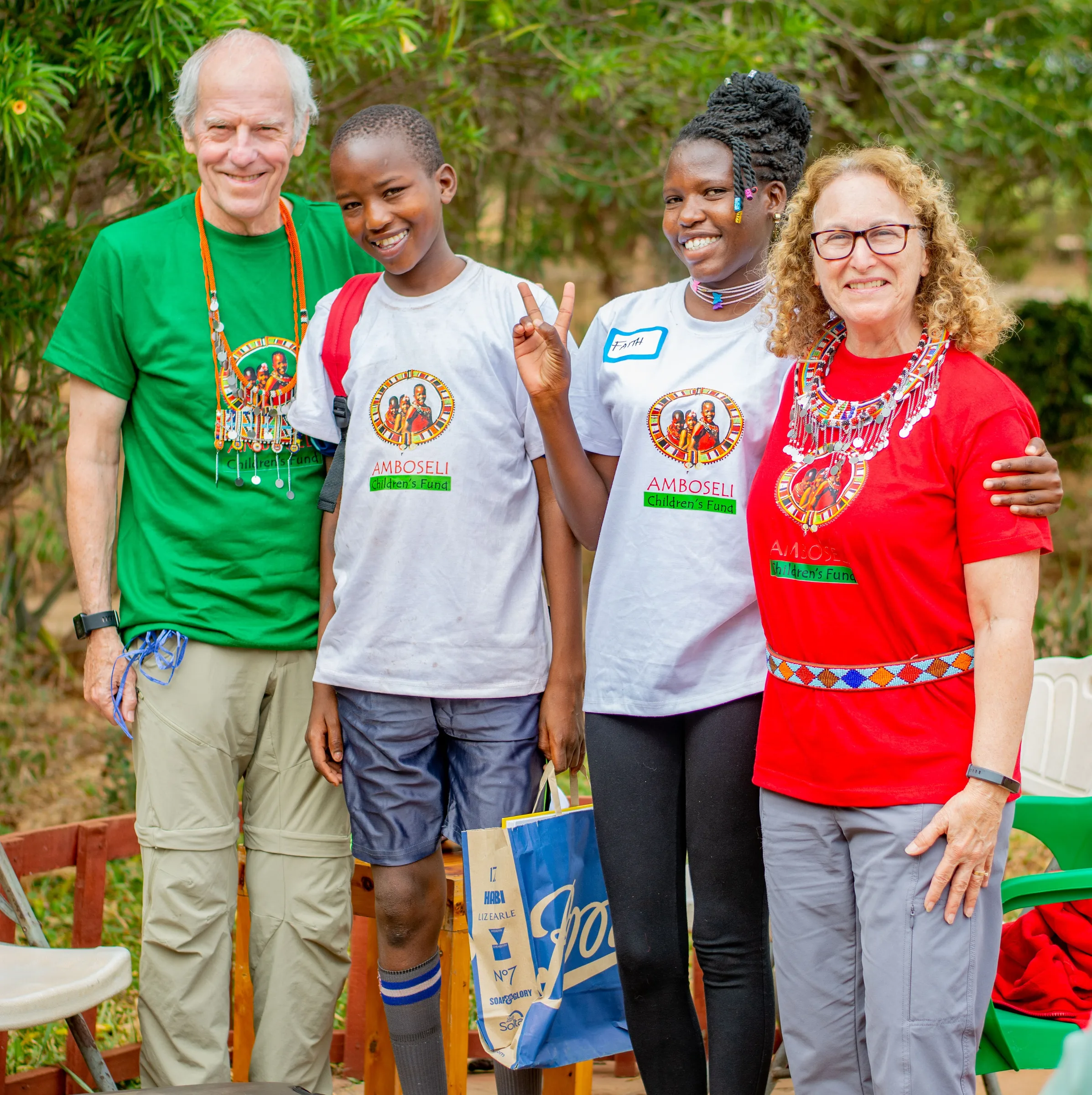 Two men and two women and a boy smile outdoors; the women wear Amboseli Children's Fund shirts